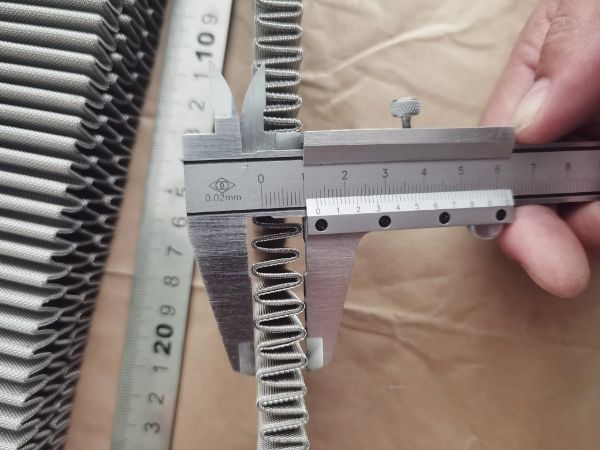 A caliper is used to measure the pleat depth of the pleated woven mesh.