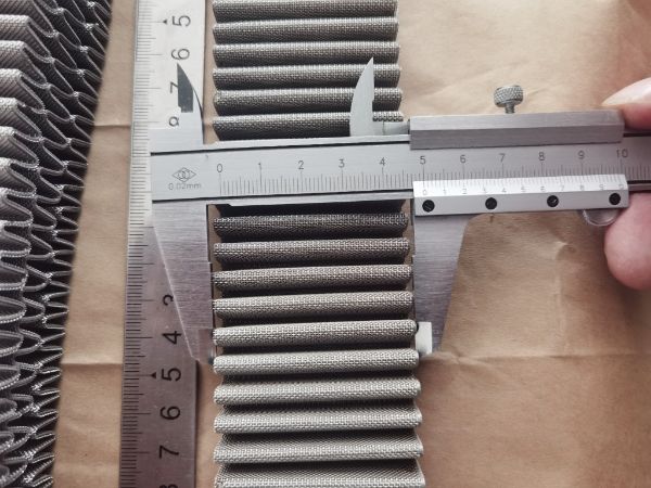 A caliper is used to measure the pleat width of the plated woven mesh.